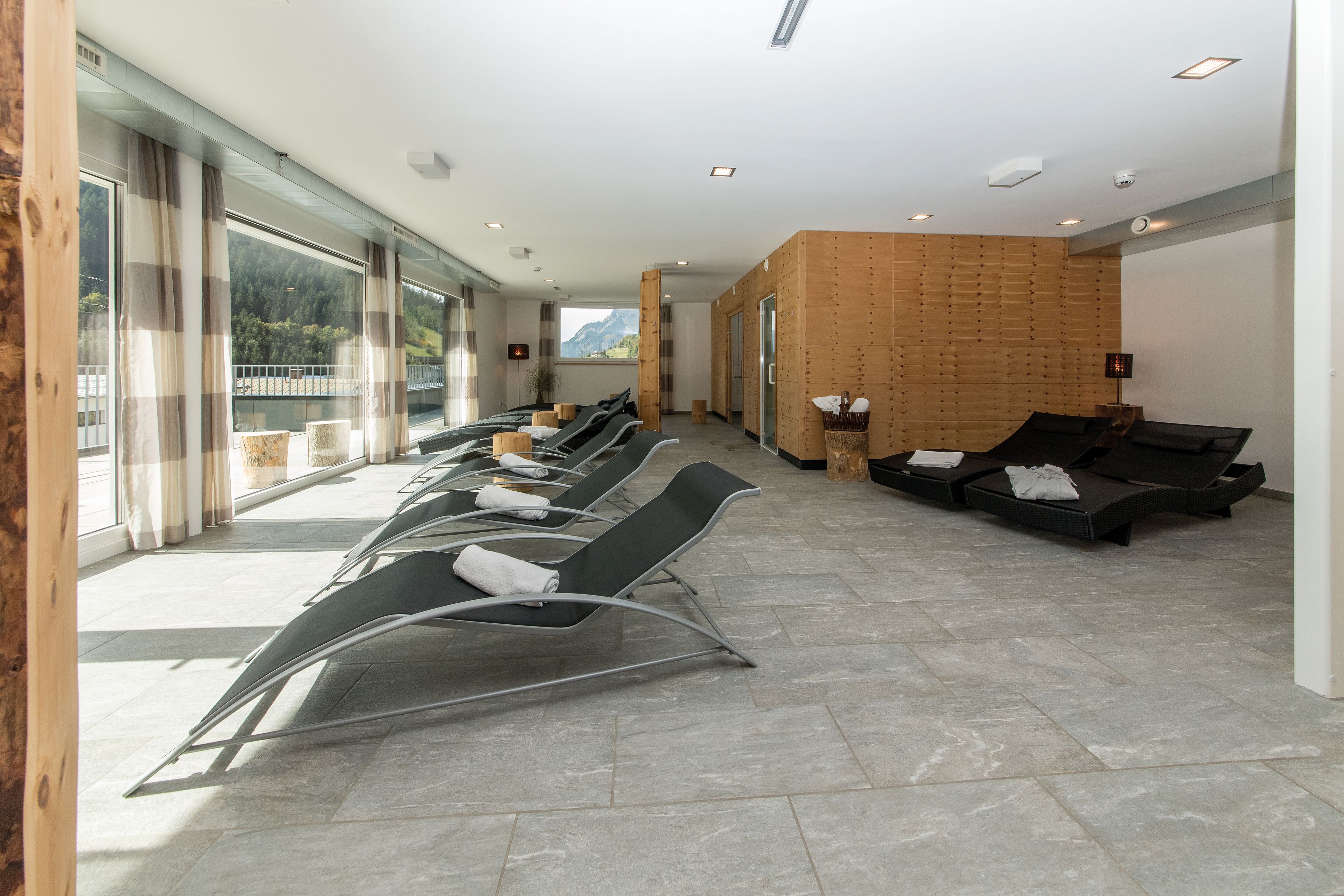 Un área de espera moderna con sillones reclinables, una pared de madera y ventanas amplias con vistas al exterior.