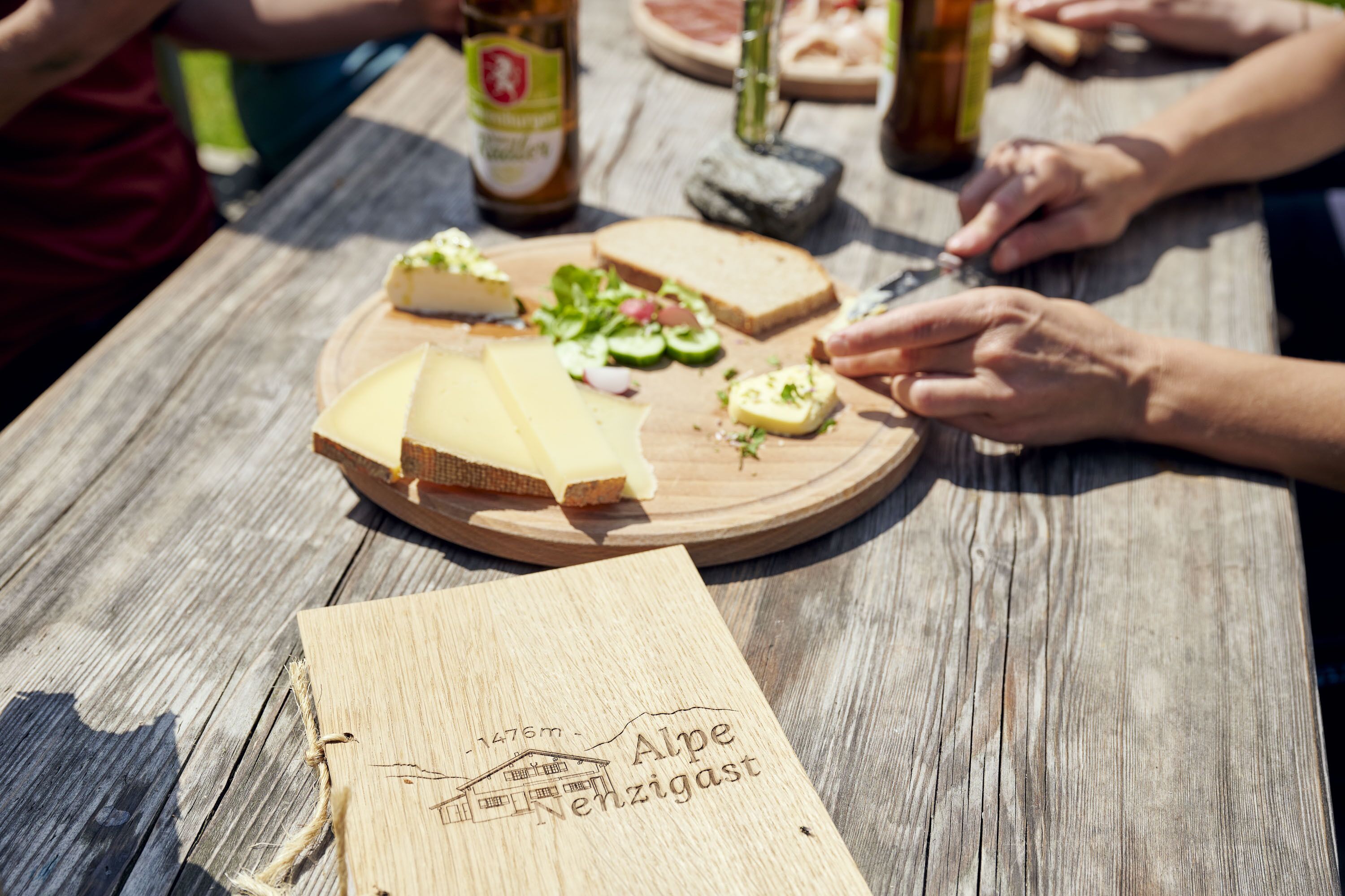 Une table en bois, sur laquelle on trouve une planche à fromage, des bouteilles et une plaque en bois.