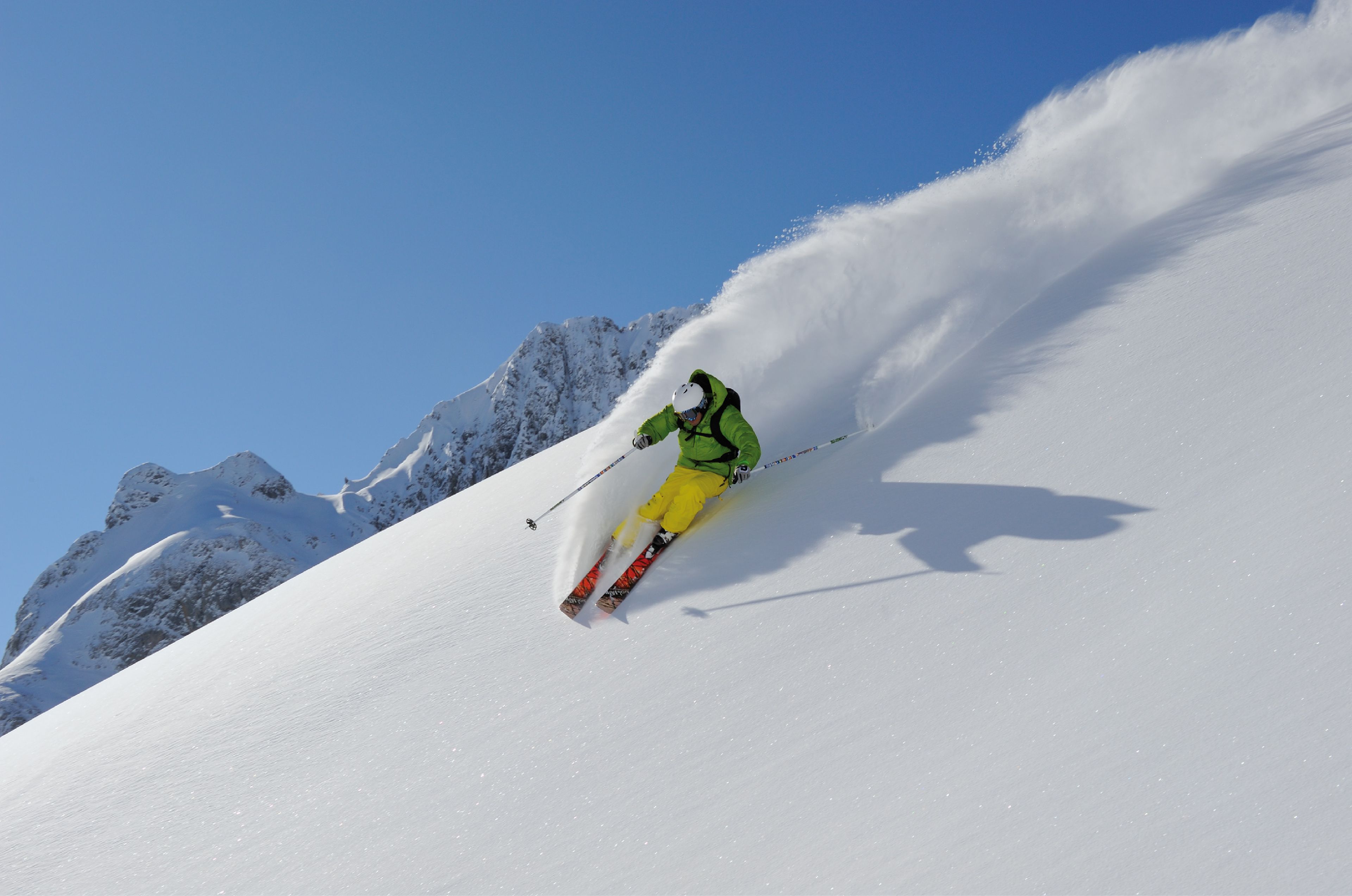 A skier on a snowy slope with a clear sky.