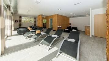 Ett modernt spa-rum med flera justerbara fåtöljer, en väggpanel i trä och ett stort fönster med utsikt över omgivningen.