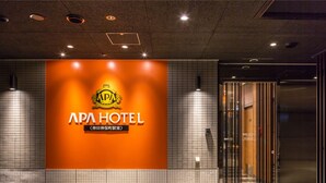 L’entrée d’un hôtel, avec une grande enseigne indiquant « APA HOTEL » et un logo au-dessus.