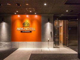 Entrada de hotel con un letrero grande que dice "APA HOTEL" y un logotipo encima.