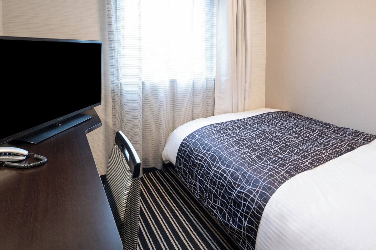 Een hotelkamer met een bed, televisie, bureau en telefoon.