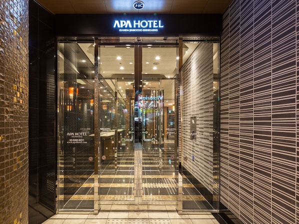 La entrada del APA HOTEL con un puerta de cristal, piso de baldosas y un letrero sobre la puerta.