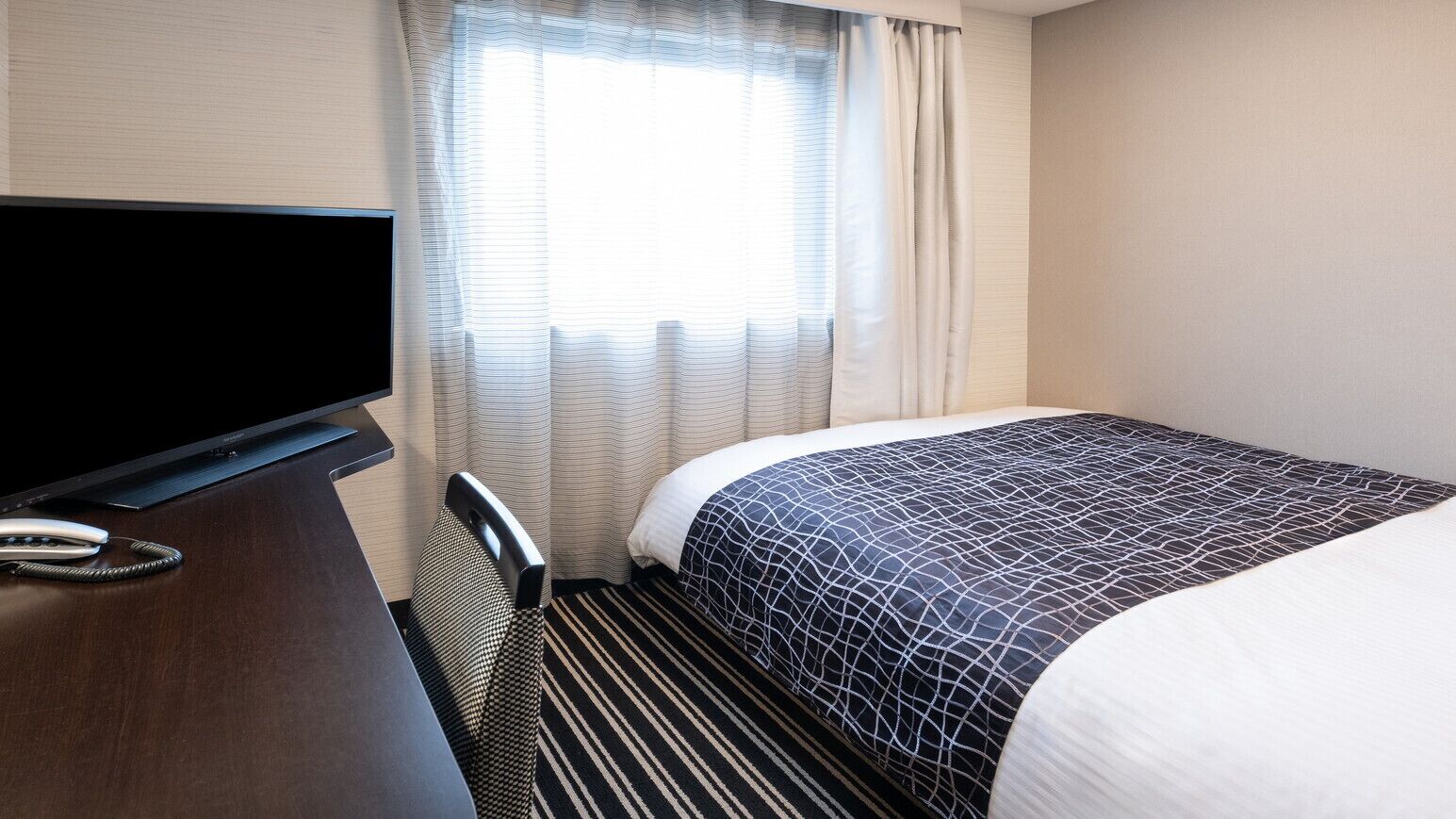 Een hotelkamer met een bed, een televisie, een bureau en een raam met gordijnen.
