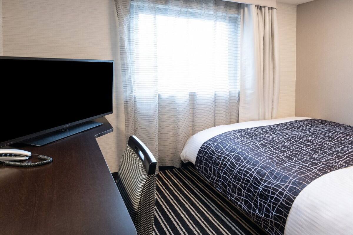 Een hotelkamer met een bed, een televisie, een bureau en een raam met gordijnen.