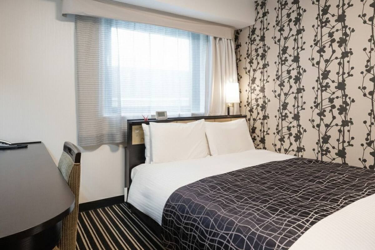 Een hotelkamer met een bed, een bureau en een raam met gordijnen.
