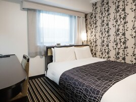 Una habitación de hotel con cama, escritorio y ventana con cortinas.