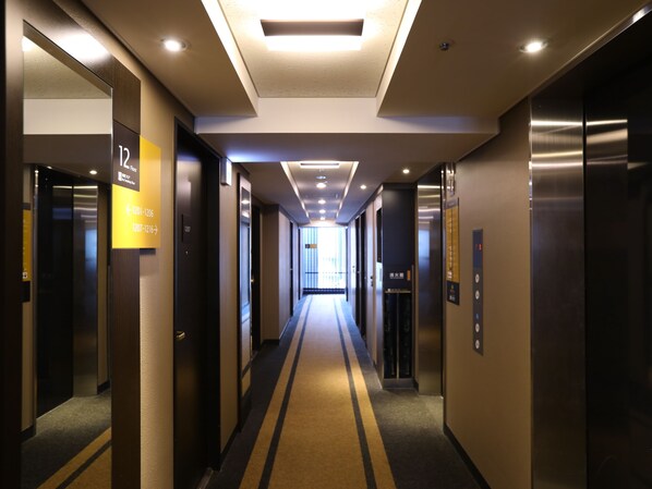 A modern hotel corridor with a central light fixture, directional signs, and a carpeted floor. - APA Hotel Kanda Jimbocho Ekihigashi (Tokyo)