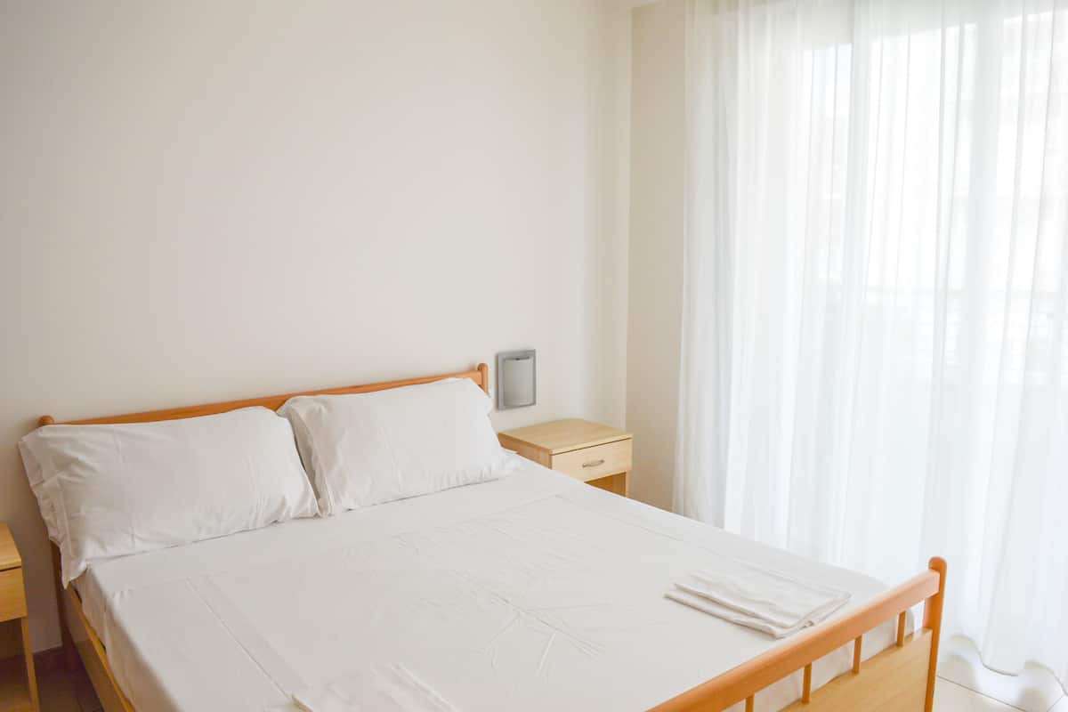 A neatly made bed with white linens in a room with a wooden headboard.
