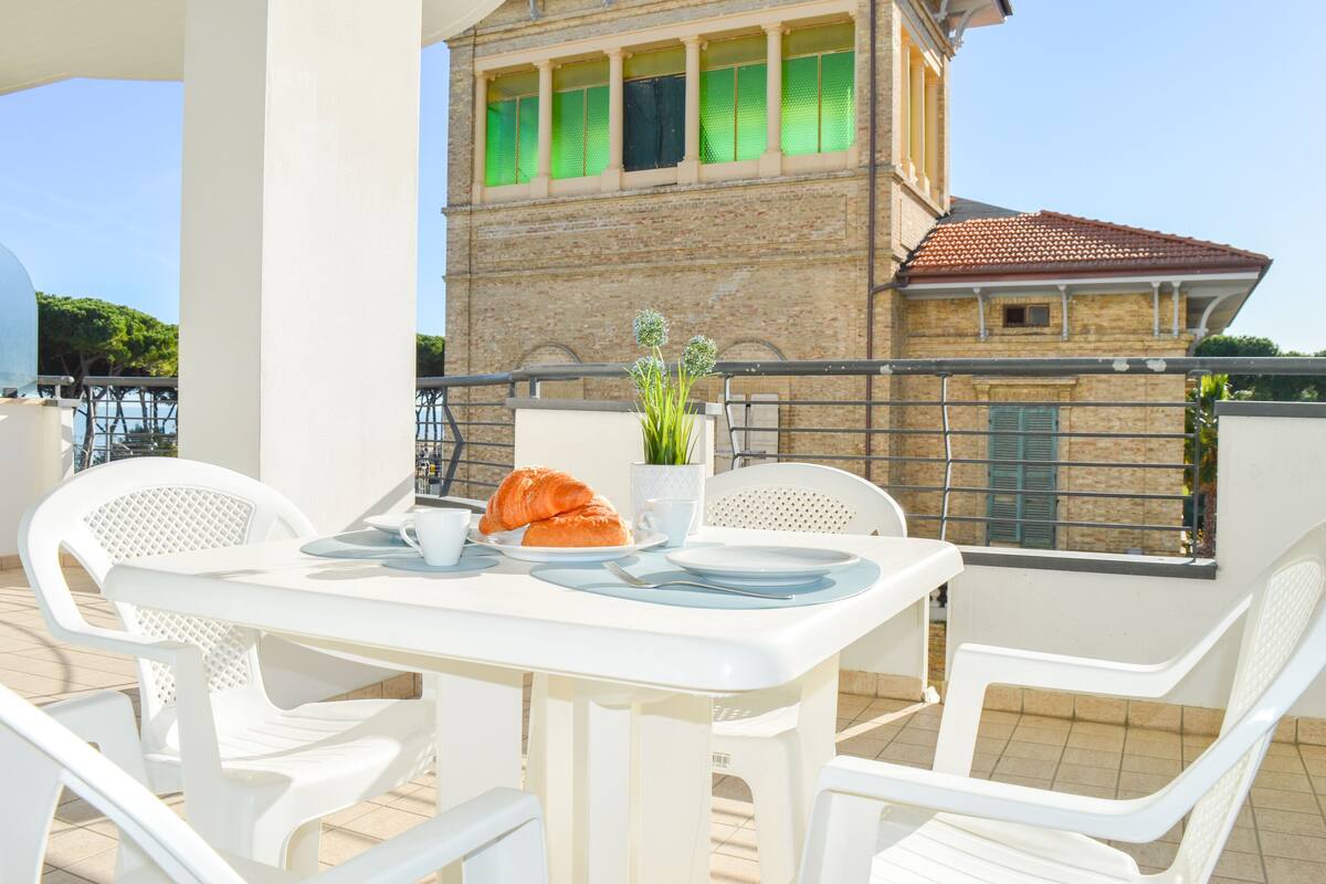 A white table with chairs on a balcony, a croissant, a cup, and a small plant.