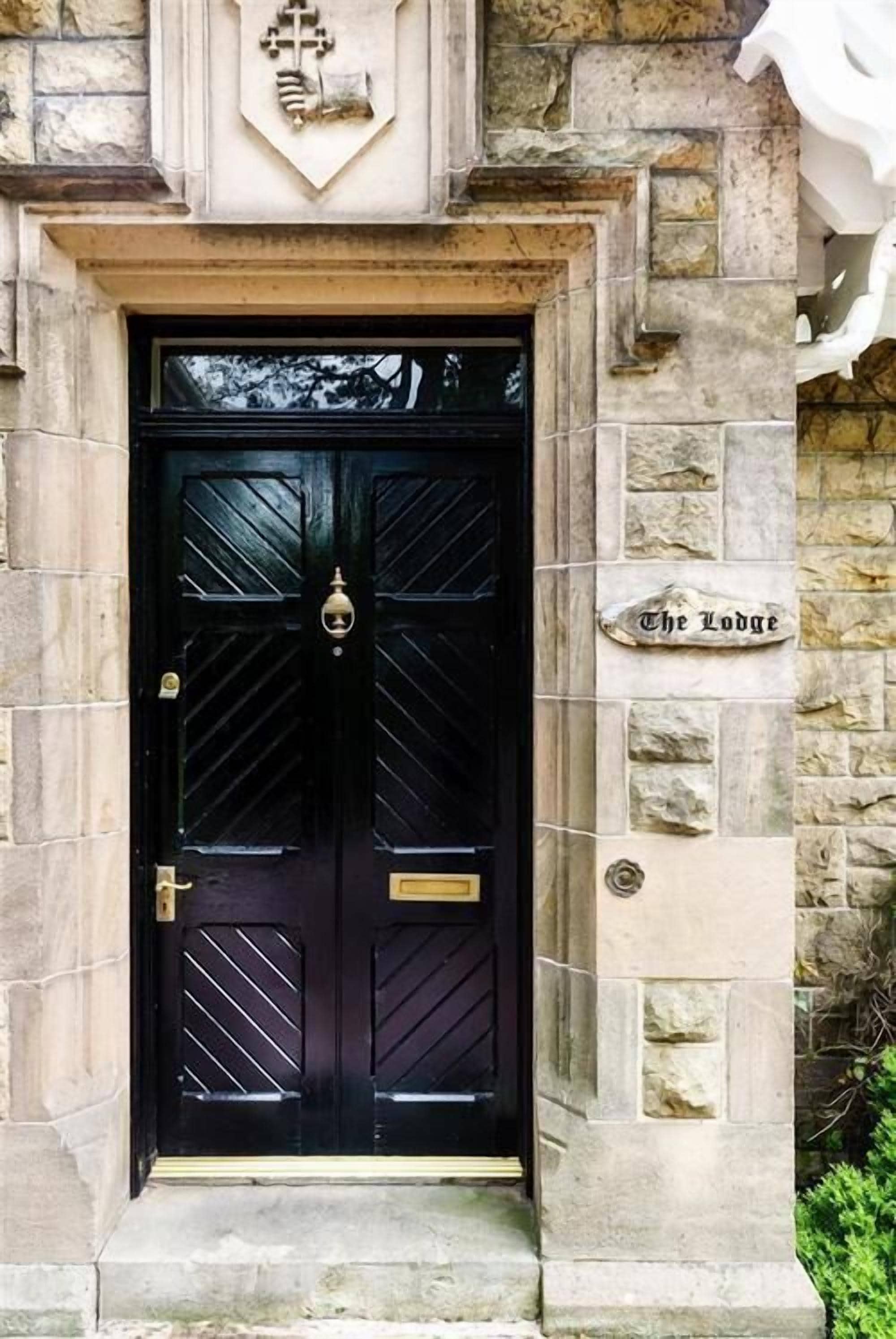 A black double door with a brass knocker, set in a stone building with a sign reading "The Lodge".