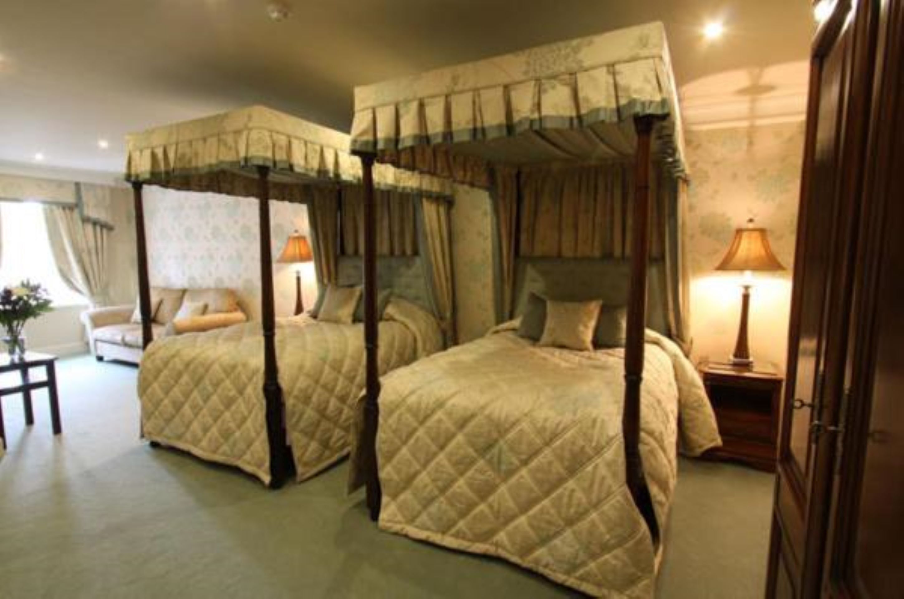 Una habitación con dos camas con dosel, una mesita de noche con lámpara y una silla.