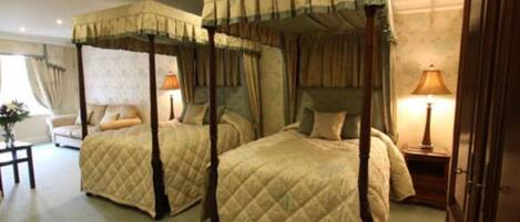 A room with two four-poster beds, a bedside table with a lamp, and a chair.