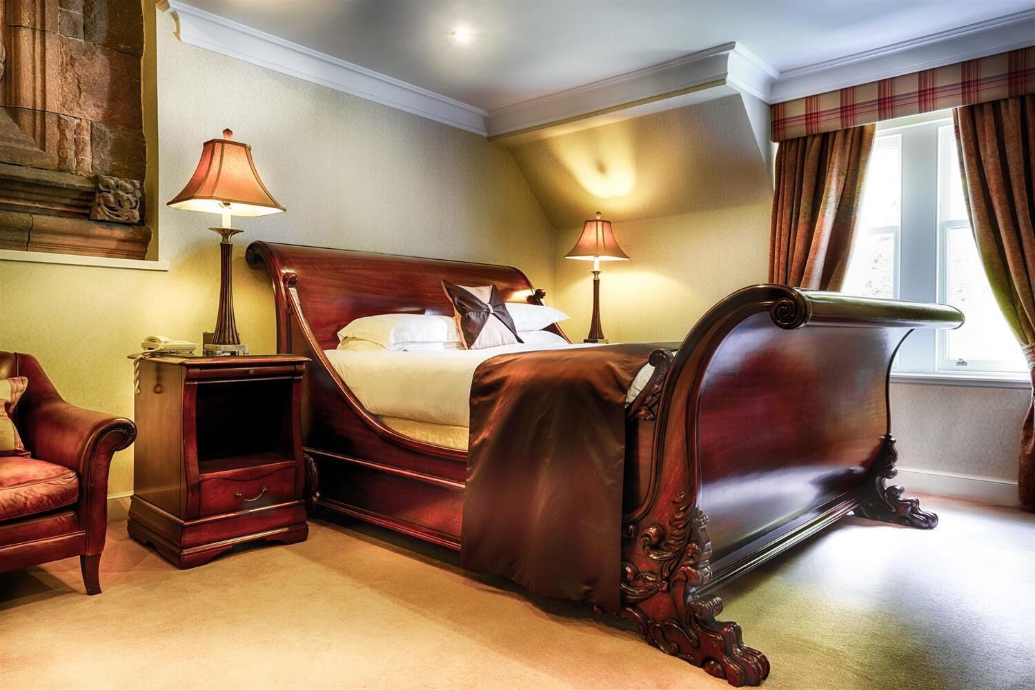 A classic bedroom with a large bed, two bedside tables, a nightstand, a chair, and a window with curtains.
