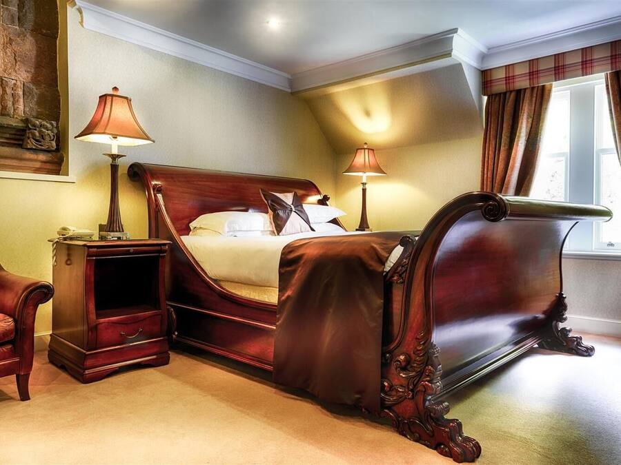 A classic bedroom with a large bed, two bedside tables, a nightstand, a chair, and a window with curtains.