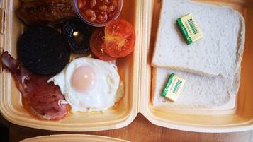 Un desayuno con tostadas, huevos, tocino, tomates, frijoles y una rebanada de morcilla.