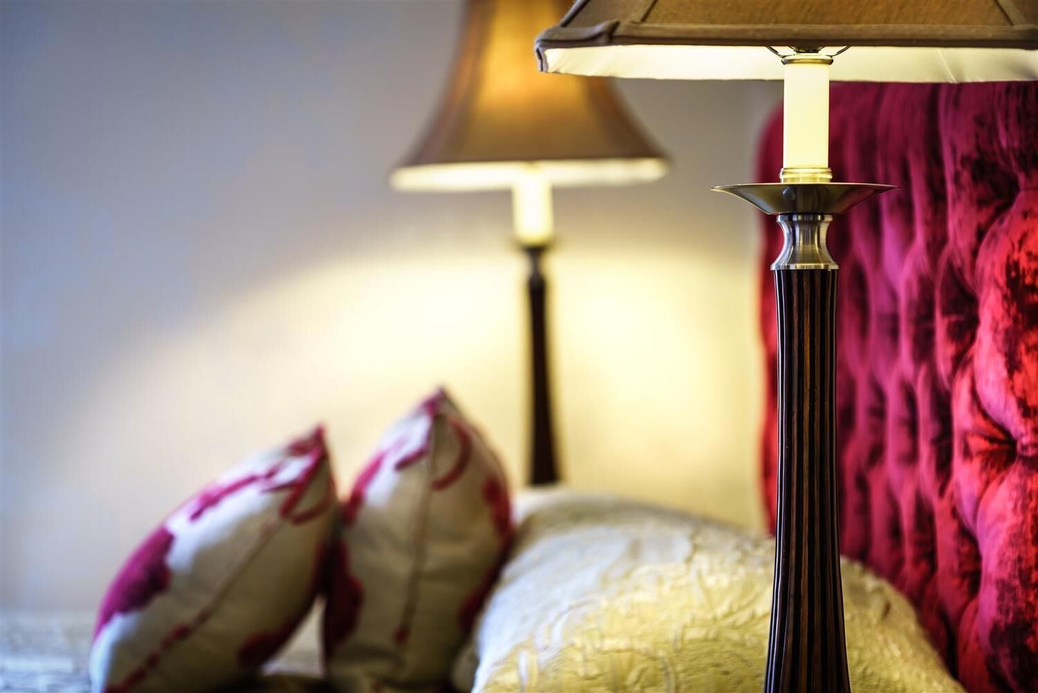 A bed with white and red pillows, a dark floor lamp, and a red curtain in the background.
