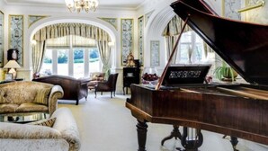 Um piano de cauda numa sala ampla, com mobiliário elegante e molduras decorativas.