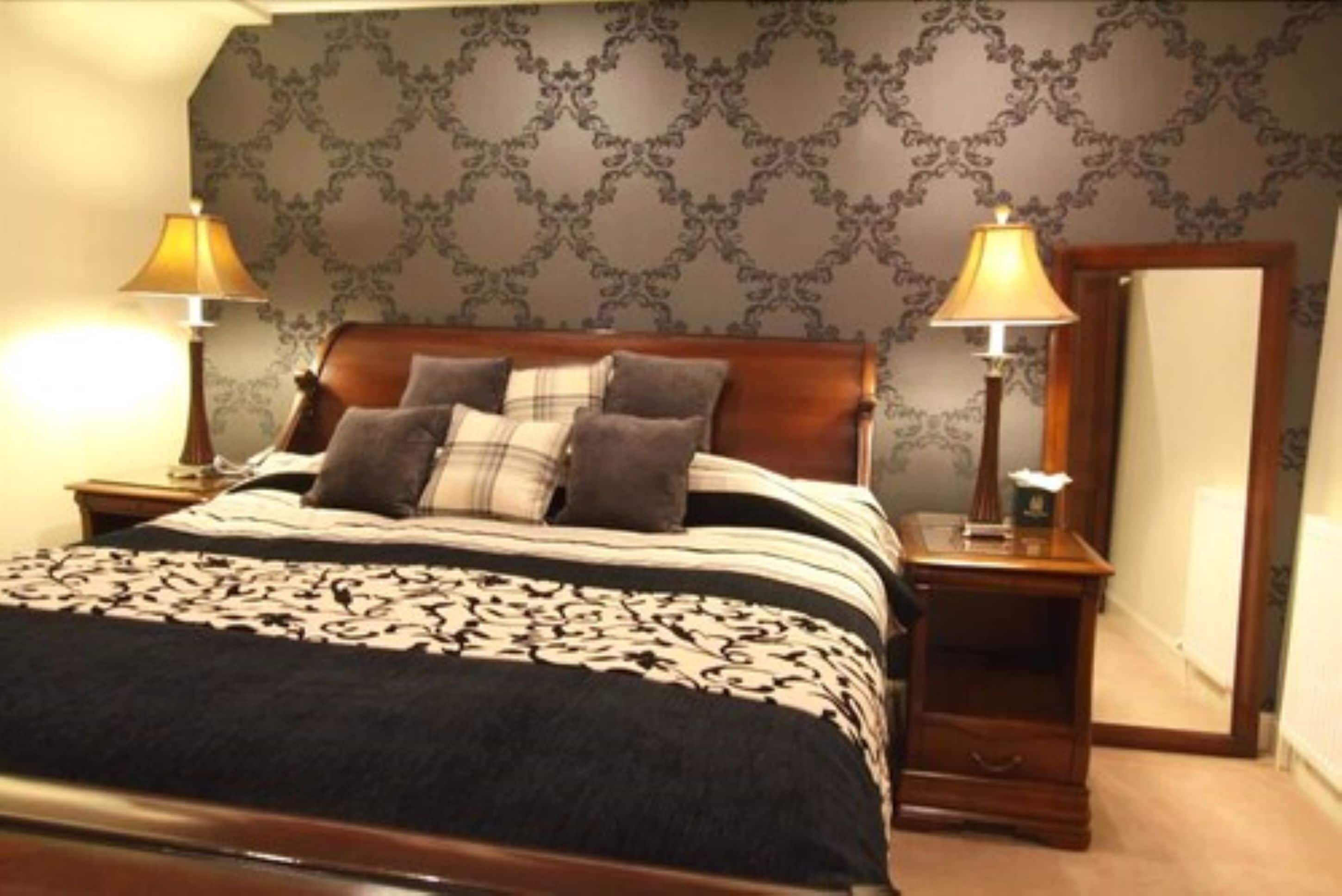 A neatly made bed with a patterned bedspread, two bedside lamps, and a mirror on the wall.