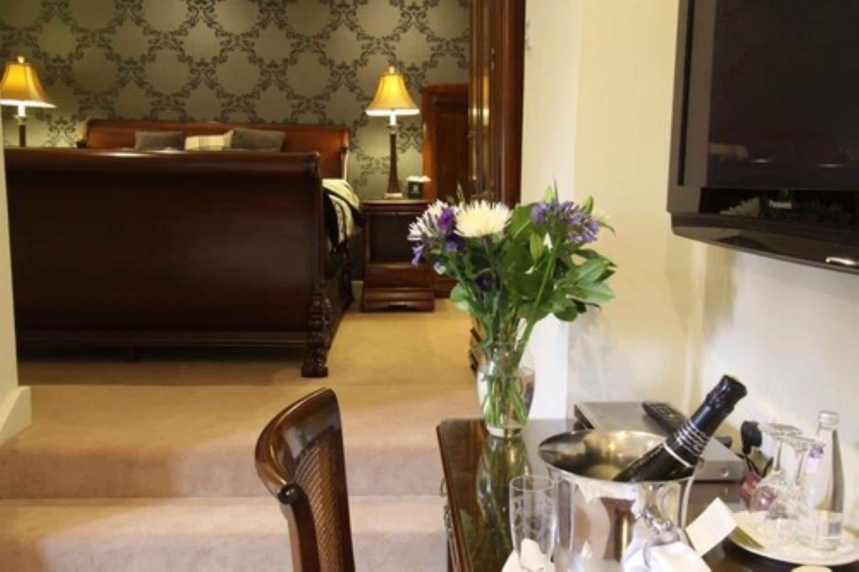 Une chambre d’hôtel avec un lit, une table à manger agrémentée d’un vase de fleurs et un téléviseur fixé au mur.