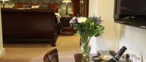 Une chambre d’hôtel avec un lit, une table à manger agrémentée d’un vase de fleurs et un téléviseur fixé au mur.