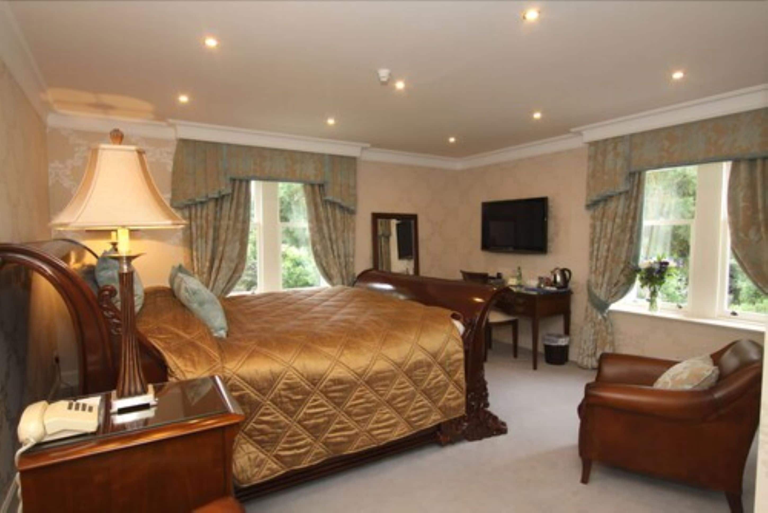 A spacious bedroom with a large bed, a desk, a chair, and a television.