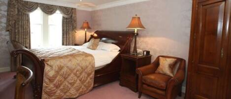 A bedroom with a large bed, two bedside lamps, a wooden wardrobe, and a leather armchair.
