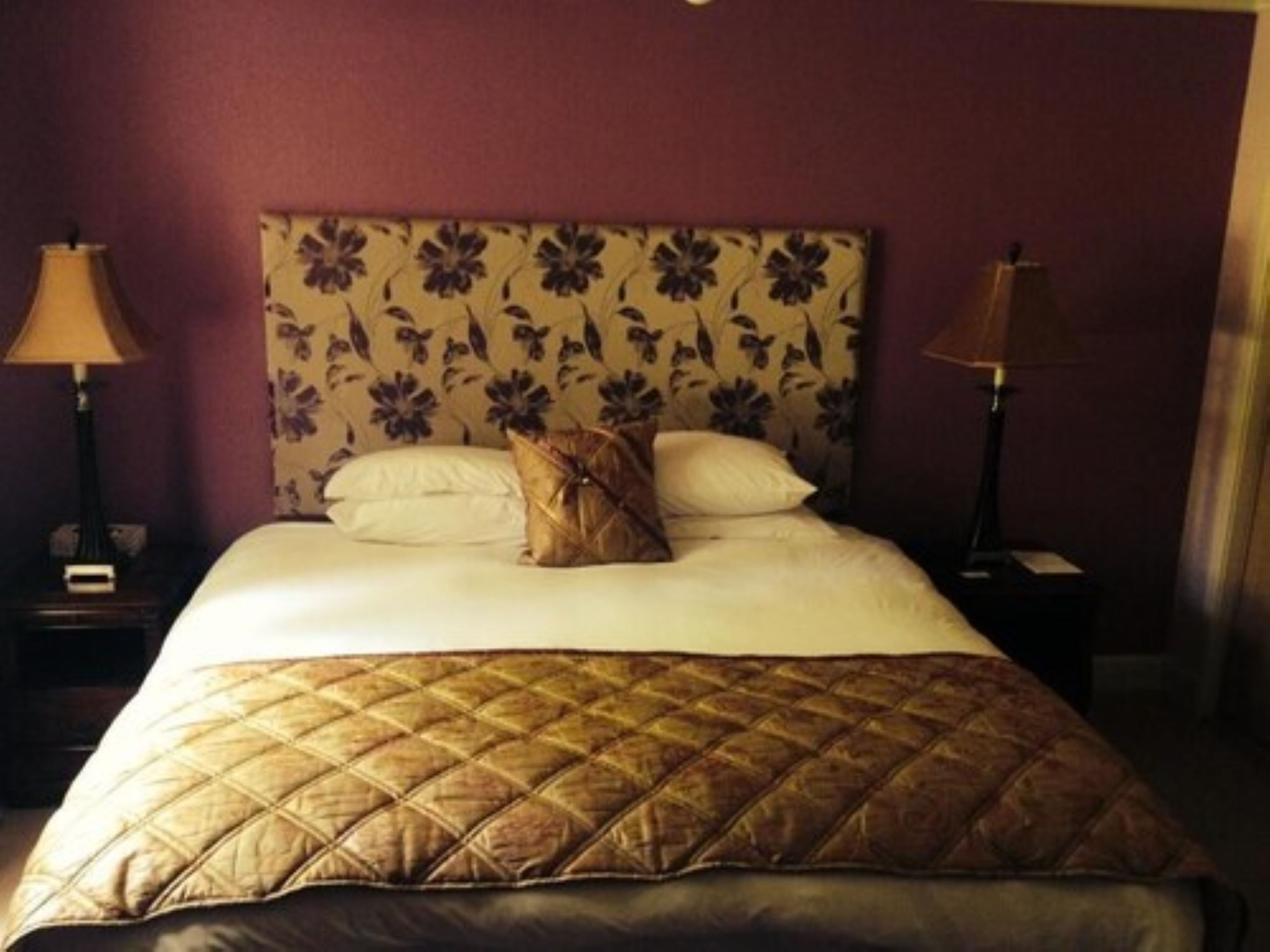 Een hotelkamer met een groot bed, een hoofdeinde met bloemenprint, twee bedlampen en een nachtkastje.