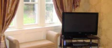A living room with a beige sofa, a television on a stand, and curtains on a window.