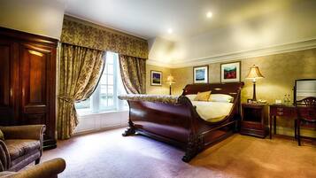 A classic bedroom with a large bed, a wooden wardrobe, a desk with a chair, and a window with curtains.