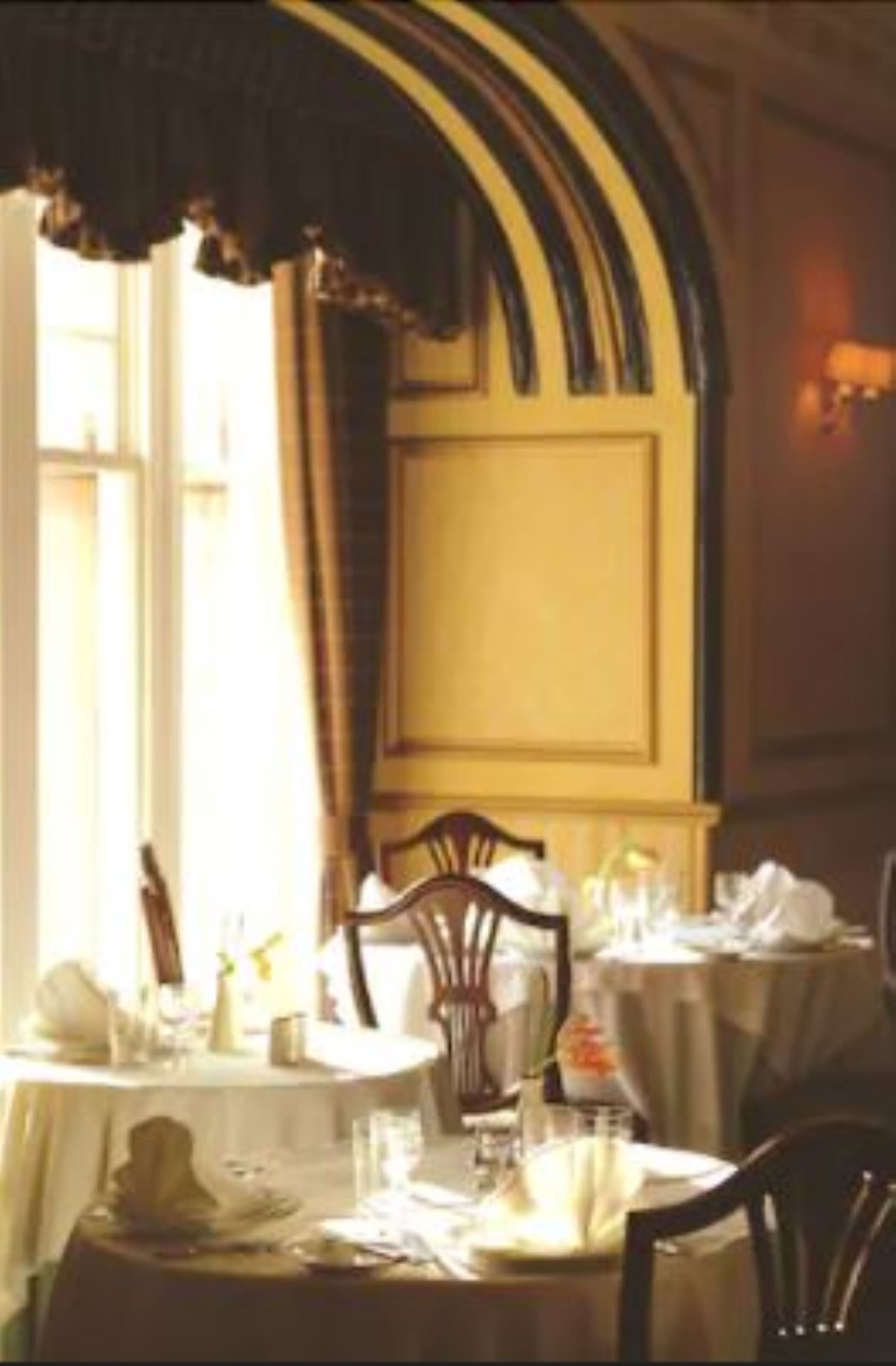 A dining area with tables set for meals, chairs, and a window with curtains.