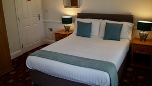 A neatly made bed with a white duvet and teal pillows, flanked by two bedside tables with lamps, a mirror above the bed, and a painting on the wall. - Old Posting House (Cockermouth)