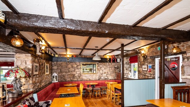 A rustic interior with stone walls, wooden beams, and a variety of seating arrangements including tables and benches. - Old Posting House (Cockermouth)