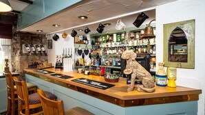 A bar with a wooden counter, several stools, and a dog sculpture. - Old Posting House (Cockermouth)