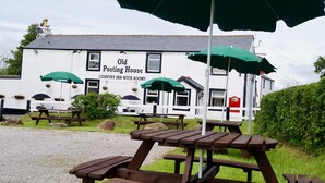 A white building with a sign reading "Old Posting House Country Inn with Rooms." There are picnic tables and green umbrellas in front. - Old Posting House (Cockermouth)