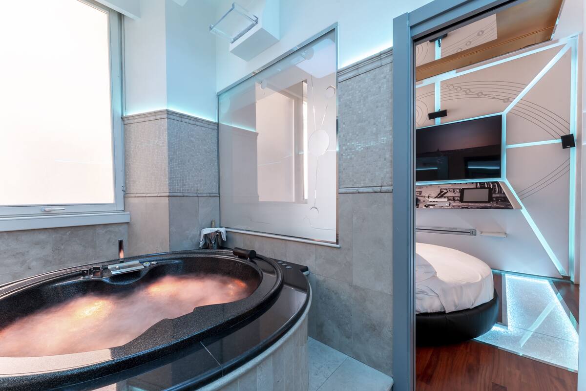 A modern bathroom with a glass-enclosed jacuzzi, a large mirror, and a built-in shower area.
