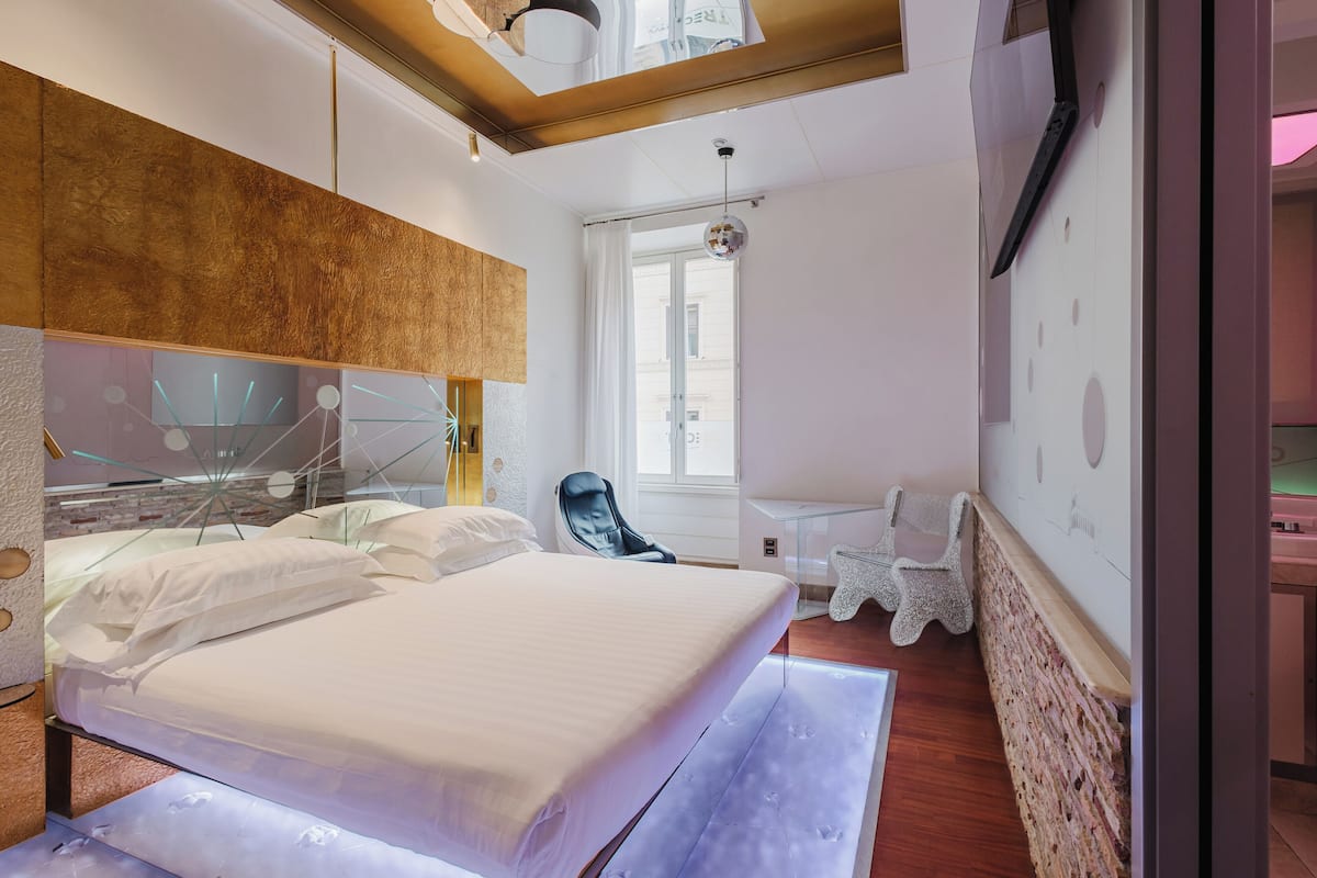 A modern bedroom with a large bed, a chair, a small table, and a window with curtains.