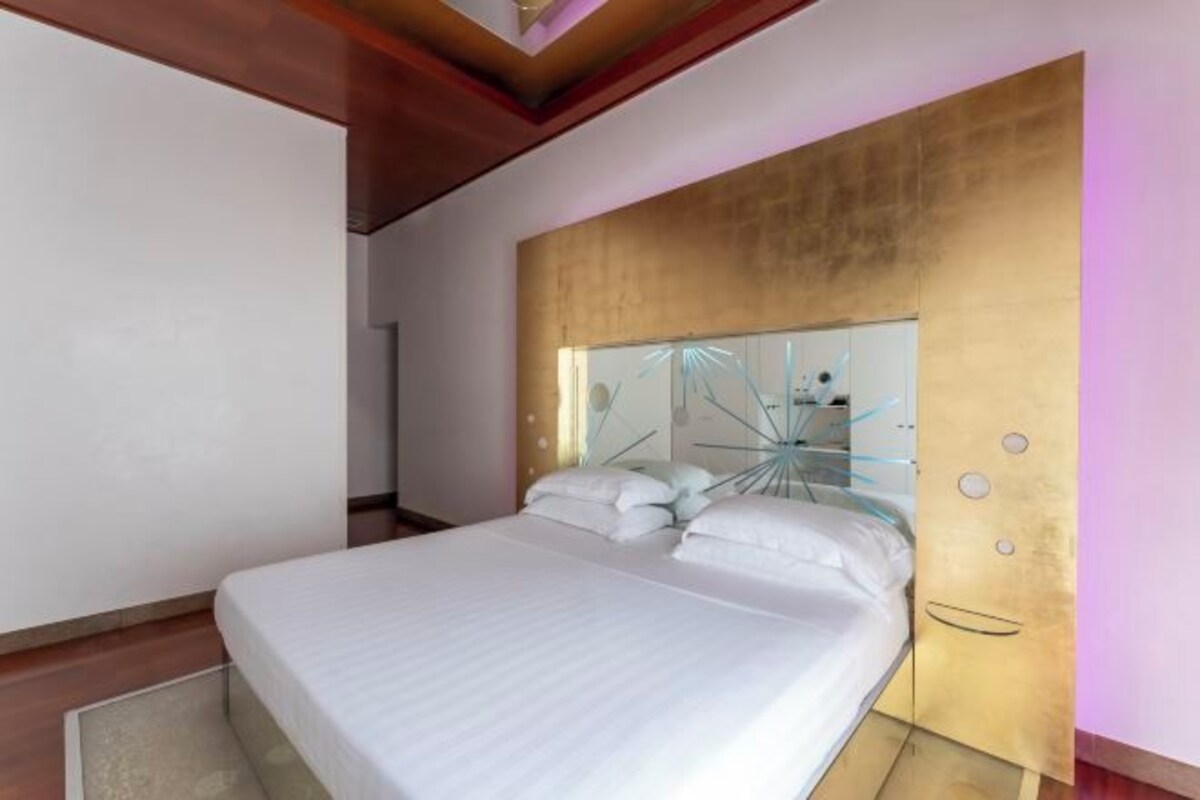 A modern bedroom with a large bed, a headboard with a unique design, and a wall-mounted light fixture.