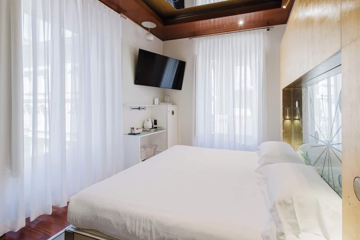 A modern hotel room with a large bed, a flat-screen TV mounted on the wall, and a glass partition with a decorative metal frame.