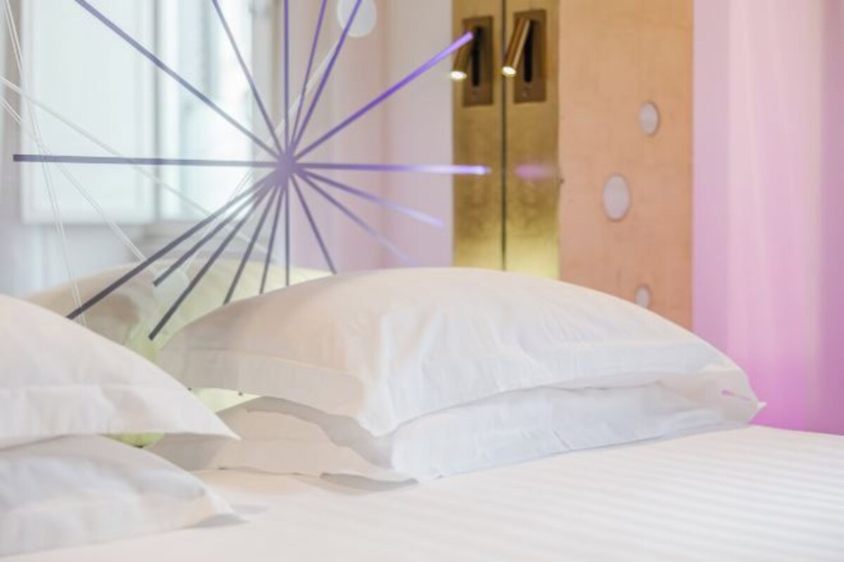 A bed with white bedding and a modern, abstract light fixture above it.