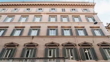 Ein mehrstöckiges Gebäude im klassischen Stil, mit gleichmäßig verteilten Fenstern mit Fensterläden, einem Balkon mit einer Brüstung und einer Straßenlaterne.
