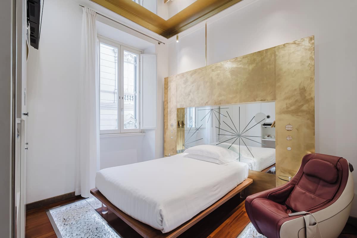 A bedroom with a bed, a massage chair, a large mirror, and a window with curtains.