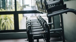 A row of black dumbbells on a rack in a gym with large windows in the background. - Amelie Hotel Manila (Manila)