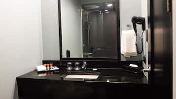 A modern bathroom with a black sink, a large mirror, a hairdryer, and toiletries.