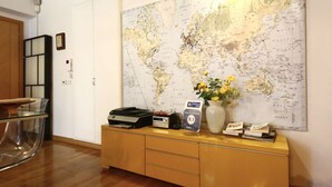 Una habitación con piso de madera, una mesa de vidrio, un mapa en la pared, un mueble con un jarrón de flores y un cartel que indica el número de habitación 9.1.