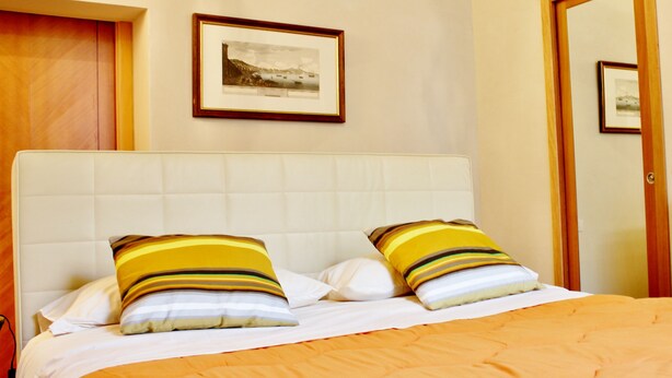 A hotel room with a large bed, two pillows, a framed picture on the wall, and a wooden door. - Talismano Luxury B&B (Naples)