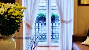 A room with a glass table, a vase of flowers, a brown leather couch, and a view through a door with white curtains. - Talismano Luxury B&B (Naples)