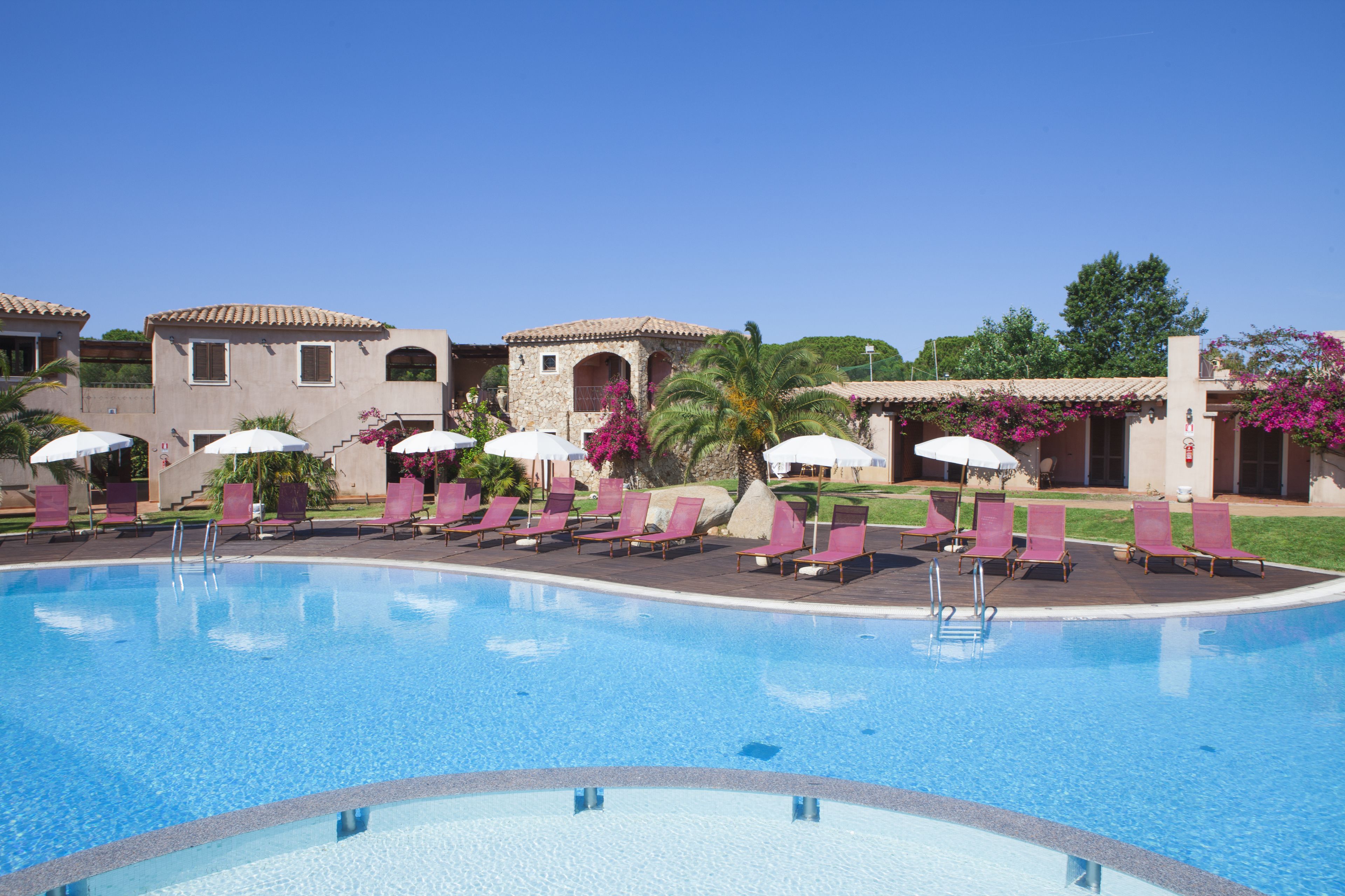 A pool area with lounge chairs and umbrellas, surrounded by buildings with a Mediterranean architectural style.