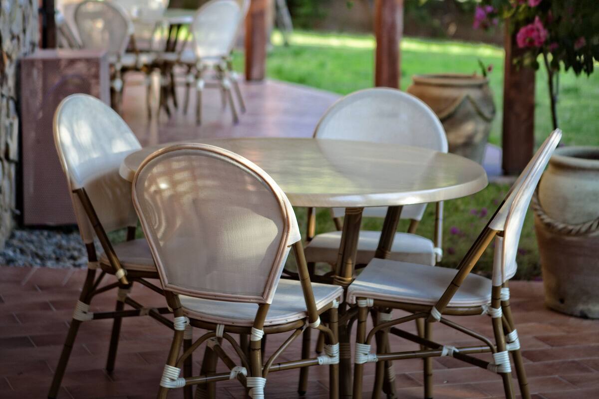Une terrasse extérieure avec une table ronde et des chaises, entourée d’une pergola et de plantes en pot.